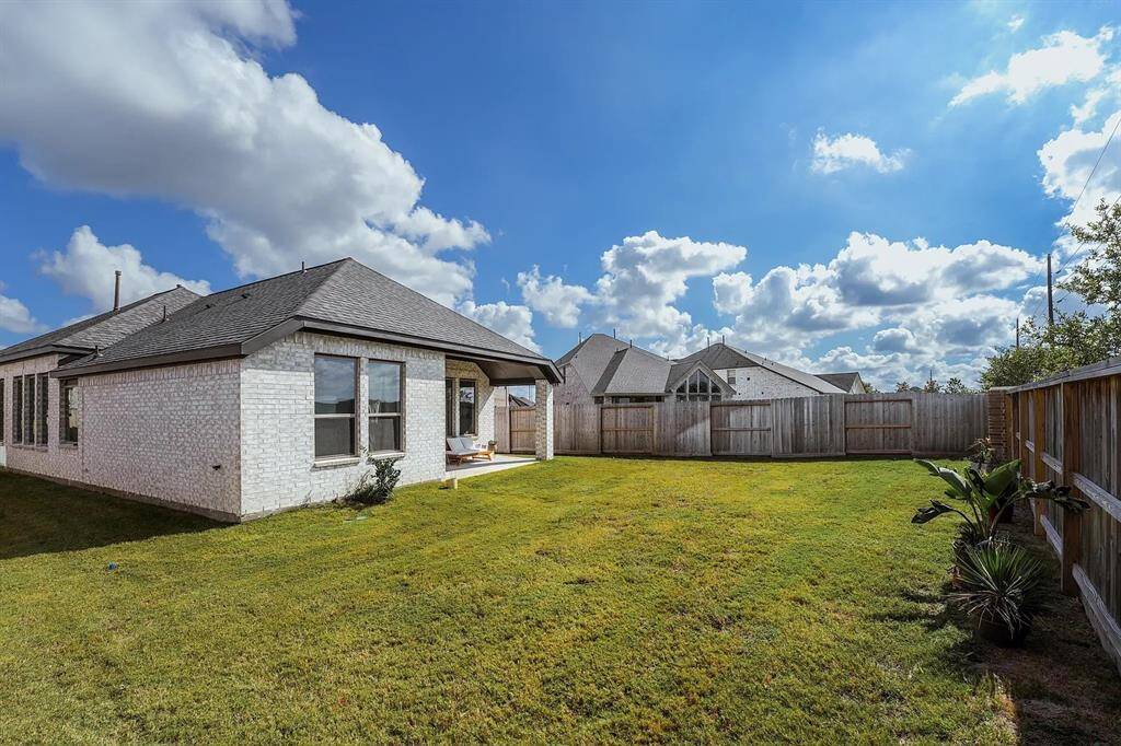 Spacious backyard with well-maintained grass, a wooden fence, and a contemporary brick home with large windows and a covered patio area, perfect for outdoor activities and relaxation.