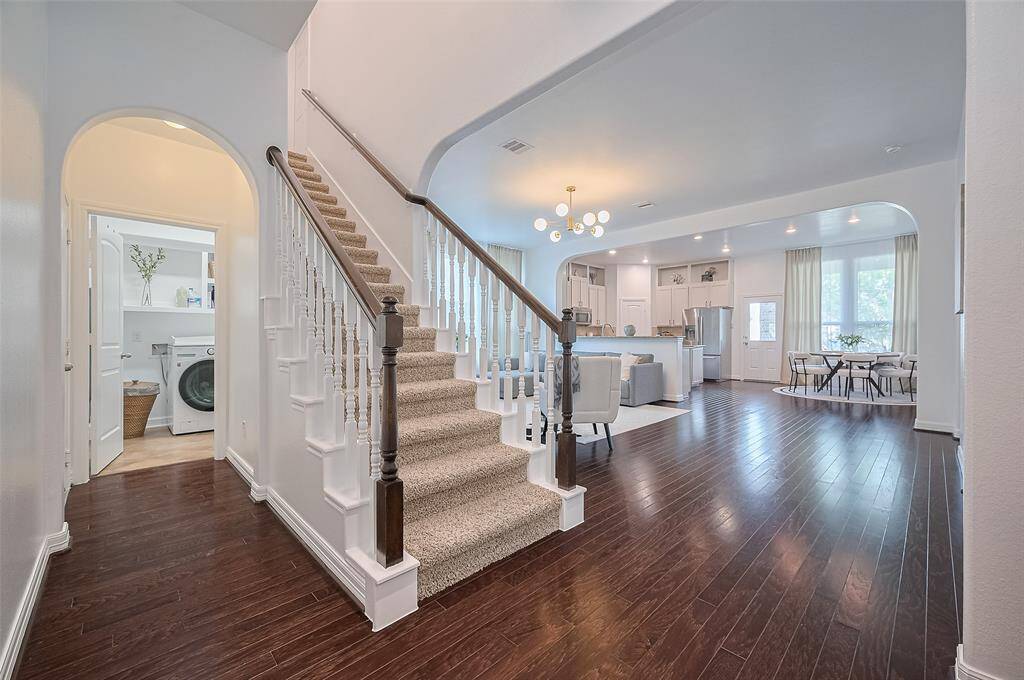 From this vantage point, the interconnectedness of daily life unfolds: the kitchen flows into the dining and living areas, anchored by wide arches. The laundry room is tucked neatly just beyond the staircase, convenient yet discreet.