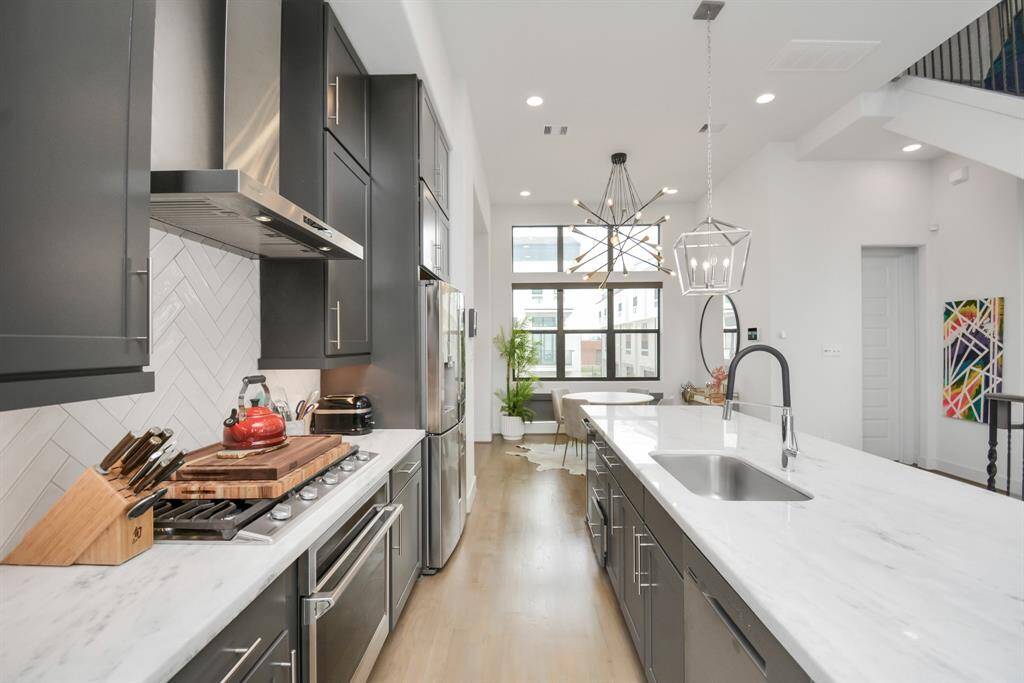 Discover a modern kitchen featuring sleek dark cabinets, stainless steel appliances, and a spacious white marble island with a sink. Large windows flood the space with natural light, creating a bright, contemporary ambiance.