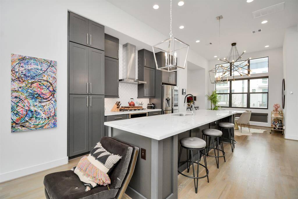Modern kitchen with sleek, dark cabinetry and a large white island featuring bar stools. High ceilings, stylish light fixtures, and ample natural light create an inviting atmosphere.  Entertainers Dream!