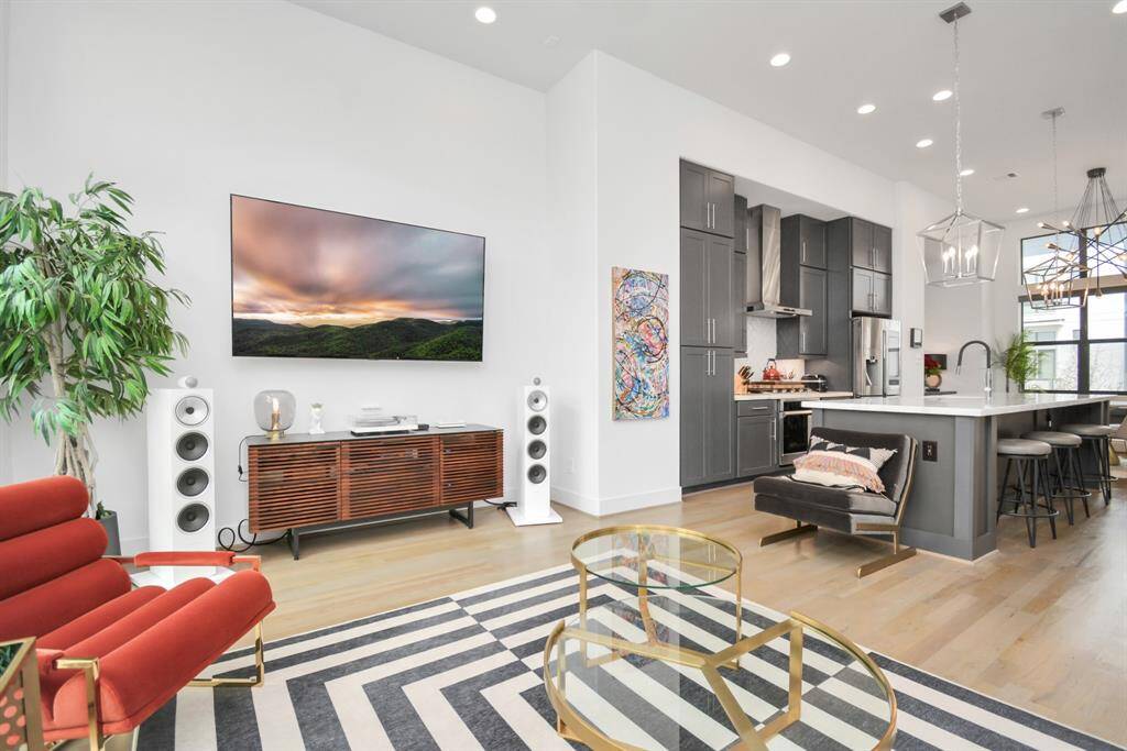 This modern open-concept living space features a sleek kitchen with dark cabinetry, a spacious island, and contemporary lighting. Large windows provide ample natural light.