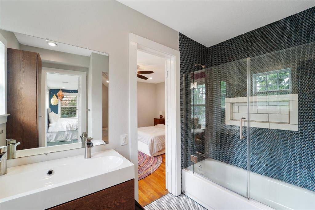 This stylish shared bathroom features a tiled shower/tub combo with a sleek glass door, elegant tile flooring, and a modern sink vanity for a polished, contemporary feel.