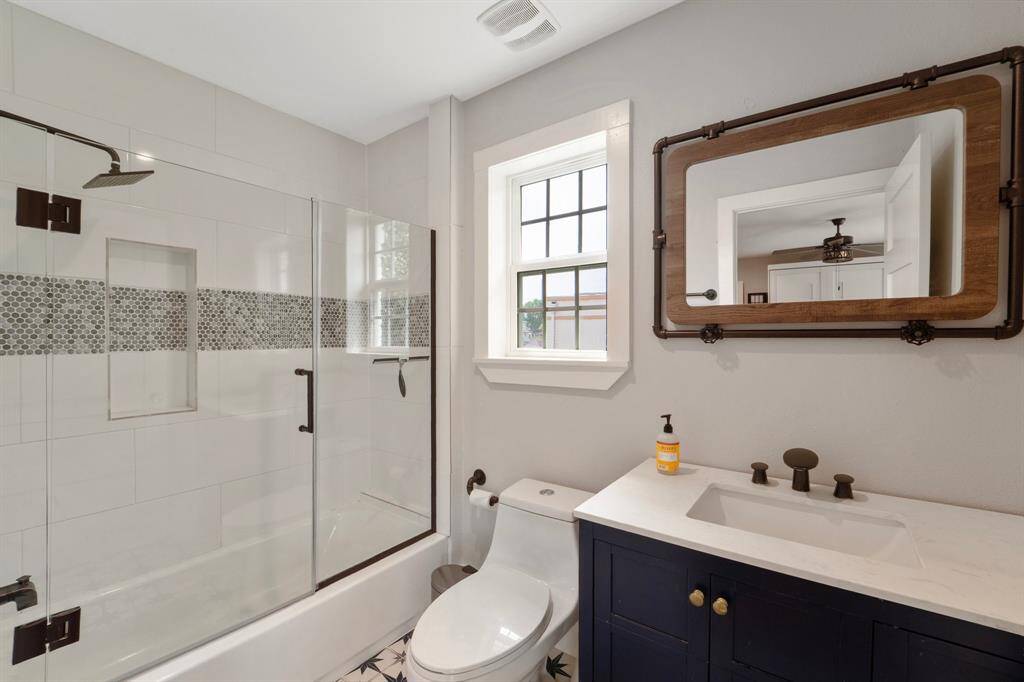The bathroom boasts a tiled shower/tub combo, a stylish vanity, and a bright window positioned above the toilet for natural light and ventilation.