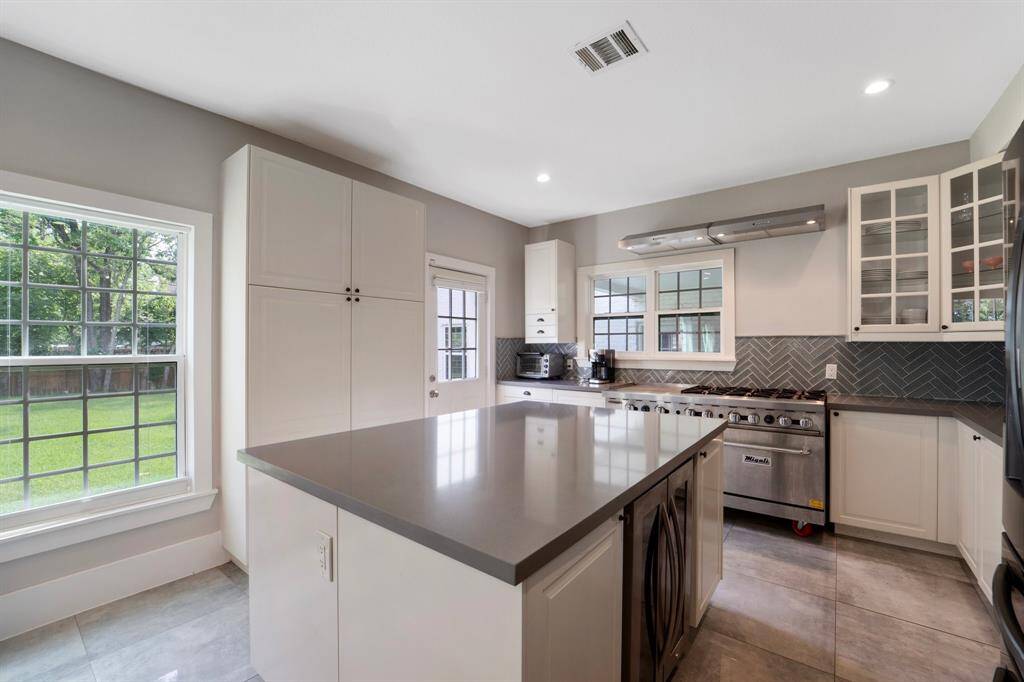 The kitchen boasts crisp white cabinetry, a large gas stove ideal for gourmet cooking, and a stylish backsplash that adds a modern, designer touch.