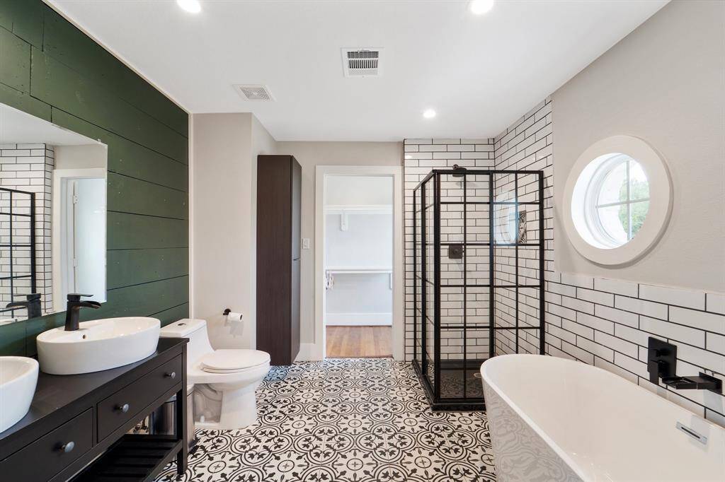 The luxurious bathroom features elegant tile flooring, a spa-like soaking bathtub, a sleek walk-in shower, and a stunning double vanity with vessel sink bowls set against a custom accent wall—perfect for unwinding in style.