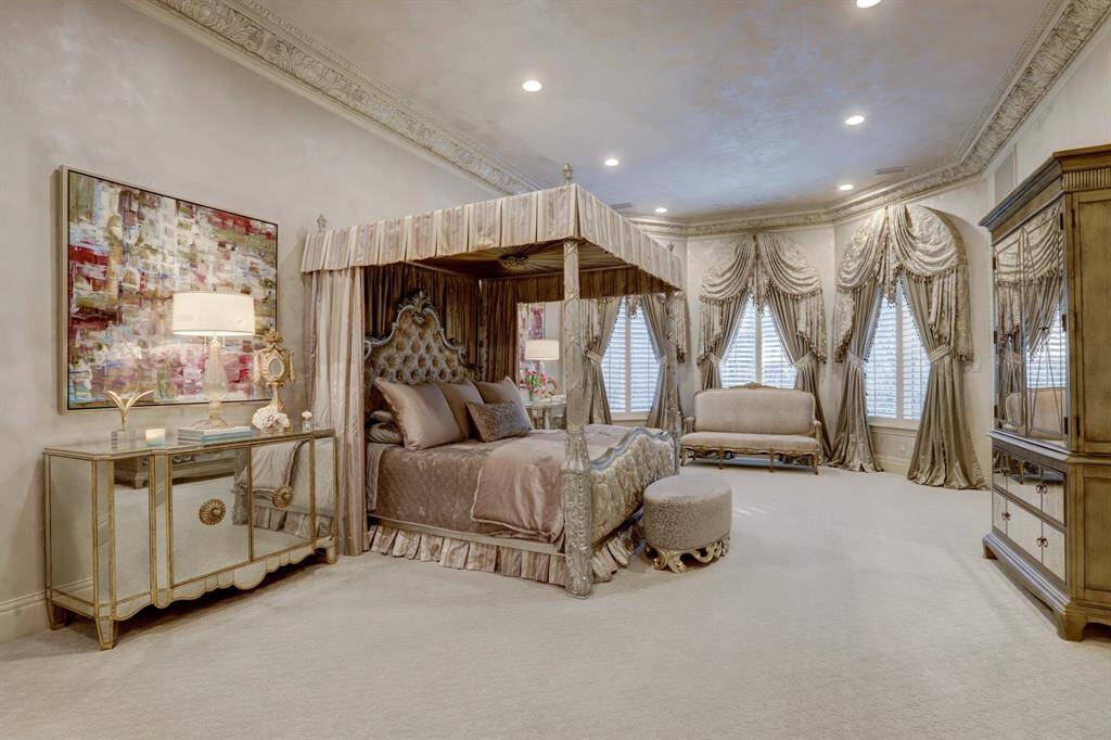 The expansive primary suite exudes elegance, showcasing custom crown molding, a spacious layout that includes a sitting area, large bay windows, and luxurious custom drapes all wrapped in gorgeous venetian plaster walls.