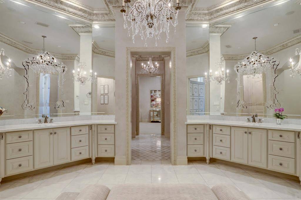 Dual vanities framed by elegant, ceiling-height mirrors, marble floors, multiple chandeliers and abundant storage space.