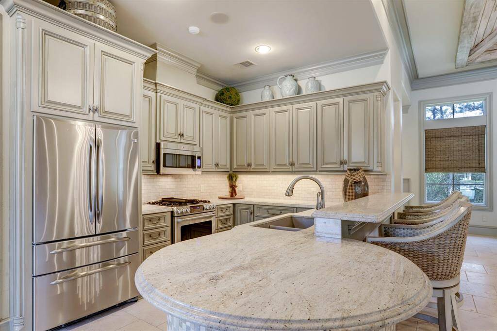 Pool house boasts a full kitchen flooded with natural light, showcasing timeless granite countertops, GE Cafe stainless steel appliances, and bar seating for added convenience.