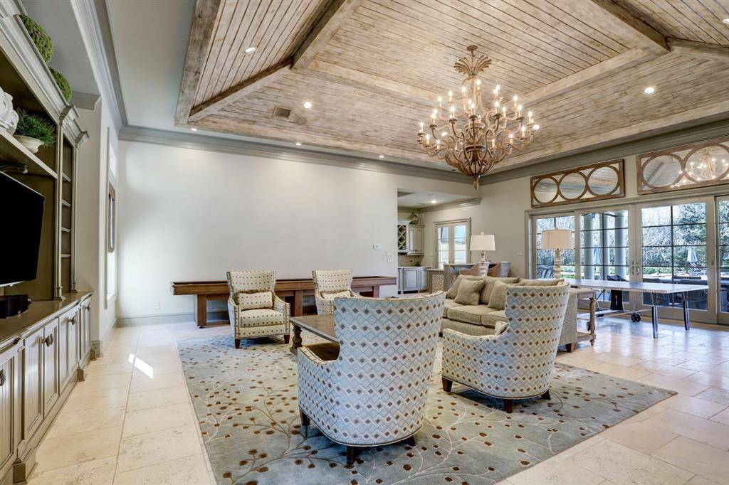 Flooded with natural light, the pool house features elegant travertine flooring, a built-in entertainment wall, and exquisite millwork on the ceiling and creates a seamless transition between the indoor and outdoor living spaces.