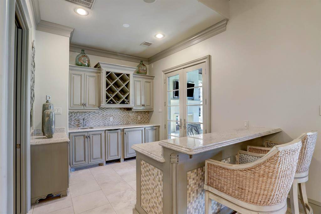 Indulge in the luxurious guest/pool house featuring a wet bar with built-in beverage storage, granite countertops, tile backsplash, bar seating, and seamless access to the veranda, ideal for entertaining and relaxation.