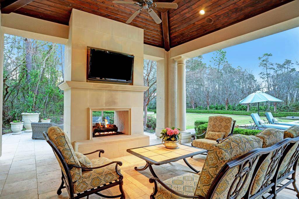 The veranda off the pool house features travertine flooring, a cozy fireplace ambiance, and outdoor seating, providing the perfect setting to admire the stunningly curated grounds and breathtaking views.