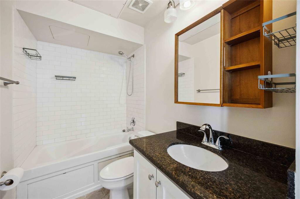 The bathroom offers a tub and shower combination, a granite countertop, and built-in storage.