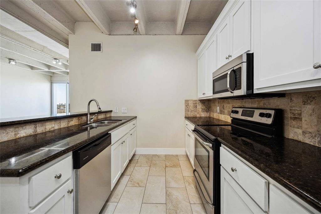 A charming galley kitchen boasts granite countertops and a decorative tile backsplash.