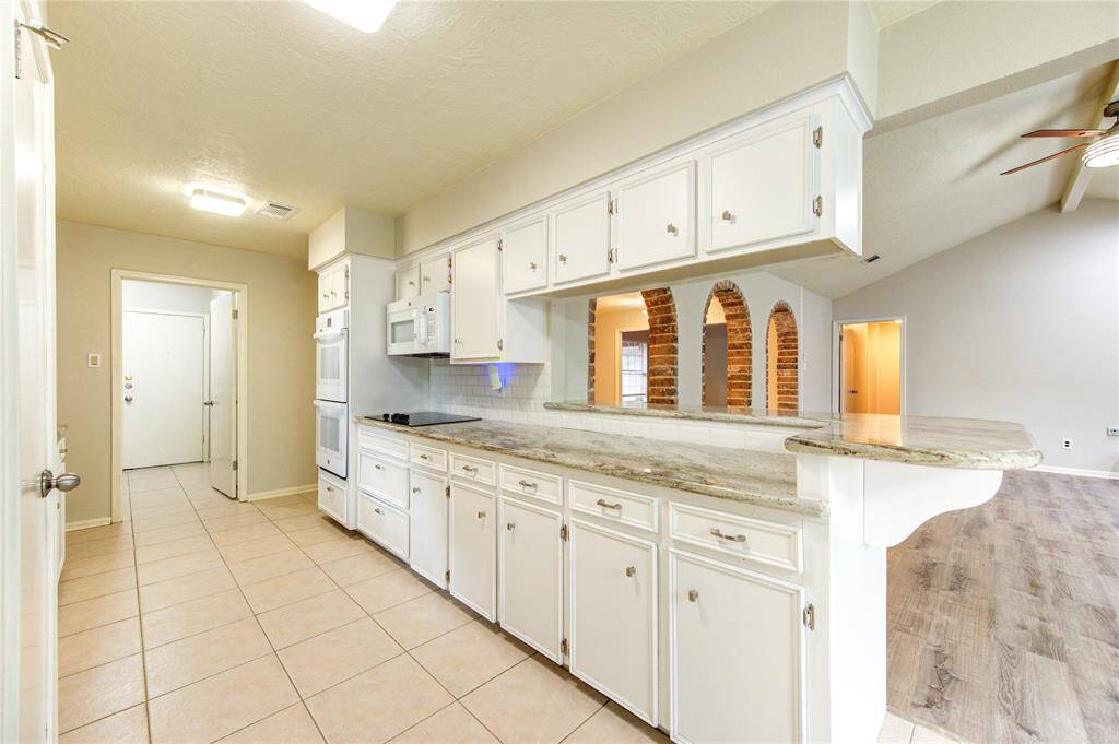 Crisp white cabinetry enhances the light and airy feel of this galley kitchen, while granite countertops pair beautifully with the tile floors in kitchen and rich vinyl plank flooring in family room.