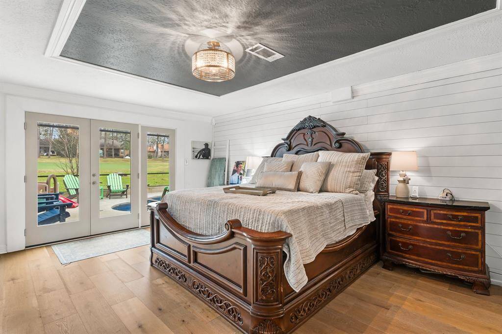 Luxurious primary bedroom with elegant flooring, a stylish chandelier, and French doors opening to a serene outdoor view.
