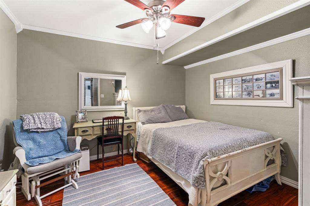 Cozy downstairs bedroom with elegant crown molding, a ceiling fan, and warm wood flooring. Ideal for guests or a home office.