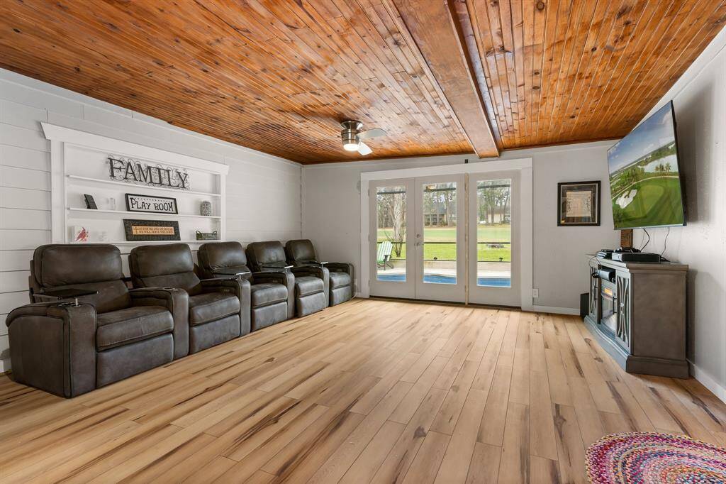 This cozy den features a warm wooden ceiling; sleek flooring and large glass doors offer a view of the indoor pool and golf course. Perfect for gatherings and relaxation.