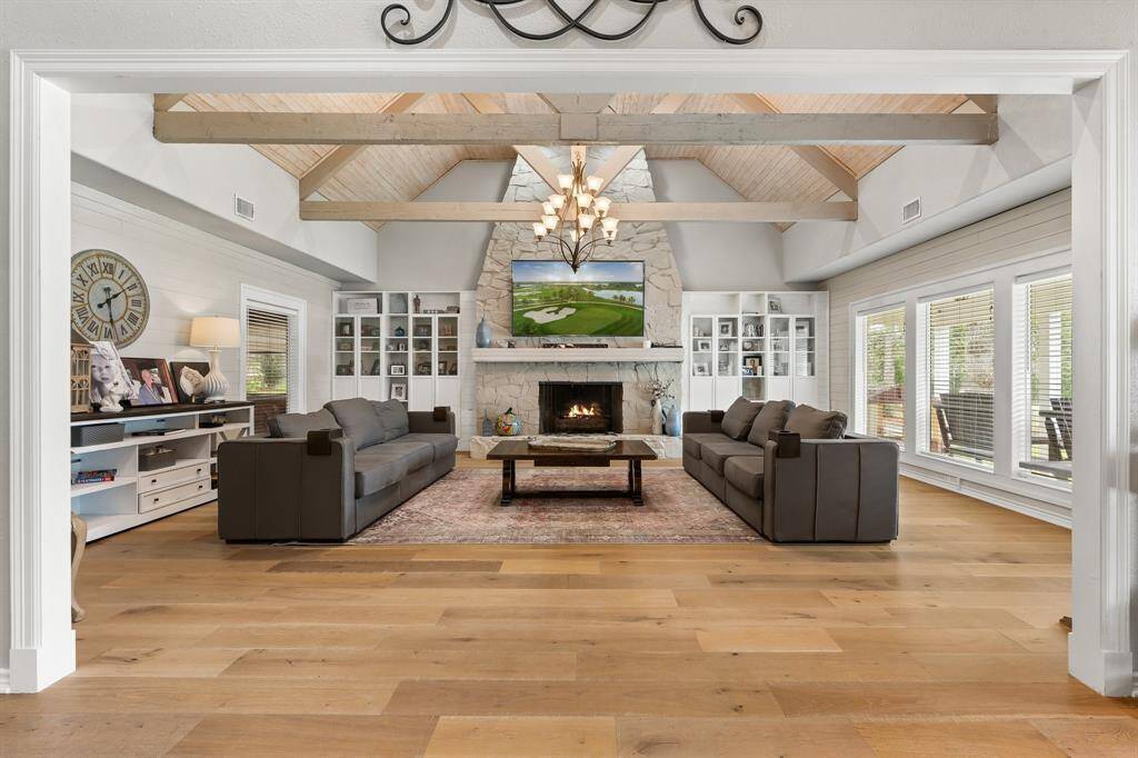 Breath taking architectural features adorn the living room...vaulted ceiling with exposed beams, a stone fireplace, and large windows offering plenty of natural light and elegant built-in shelving.