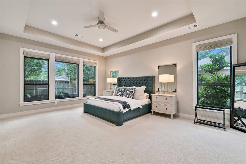 Oversized primary bedroom with tray ceiling, recessed lighting, modern fan, sitting area and overlooks backyard.