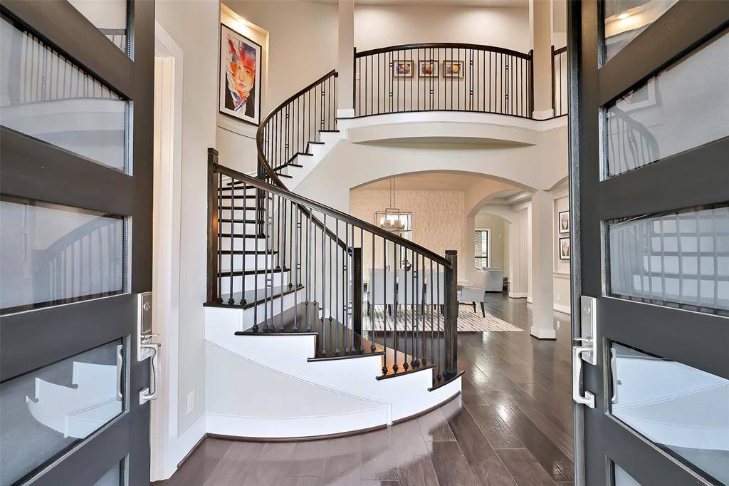 Foyer showcases high ceilings, double glass front doors, wide plank wood flooring and an elegant sweeping staircase.
