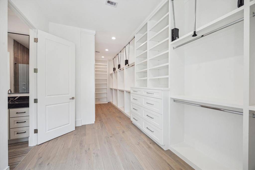Spacious primary closet features built-in storage and ample room for hanging clothes with pull-down bars for accessing all custom storage solutions.