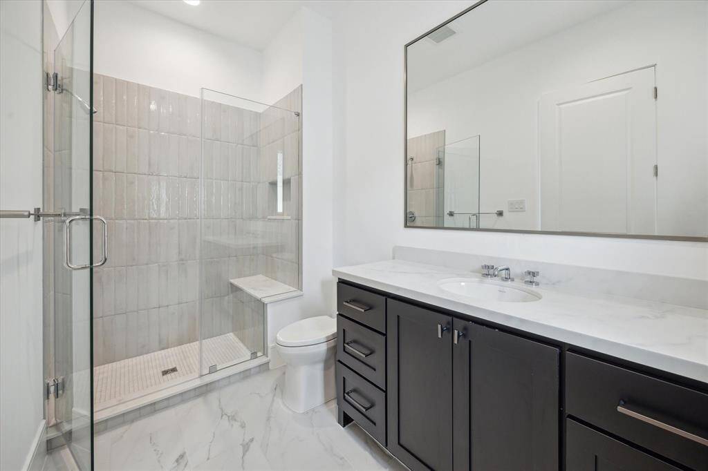 En-suite bath features glass-enclosed freestanding shower lined with Maniscalco Contour glossy tiles, Quartz countertops, and large vanity area with under-cabinet storage.