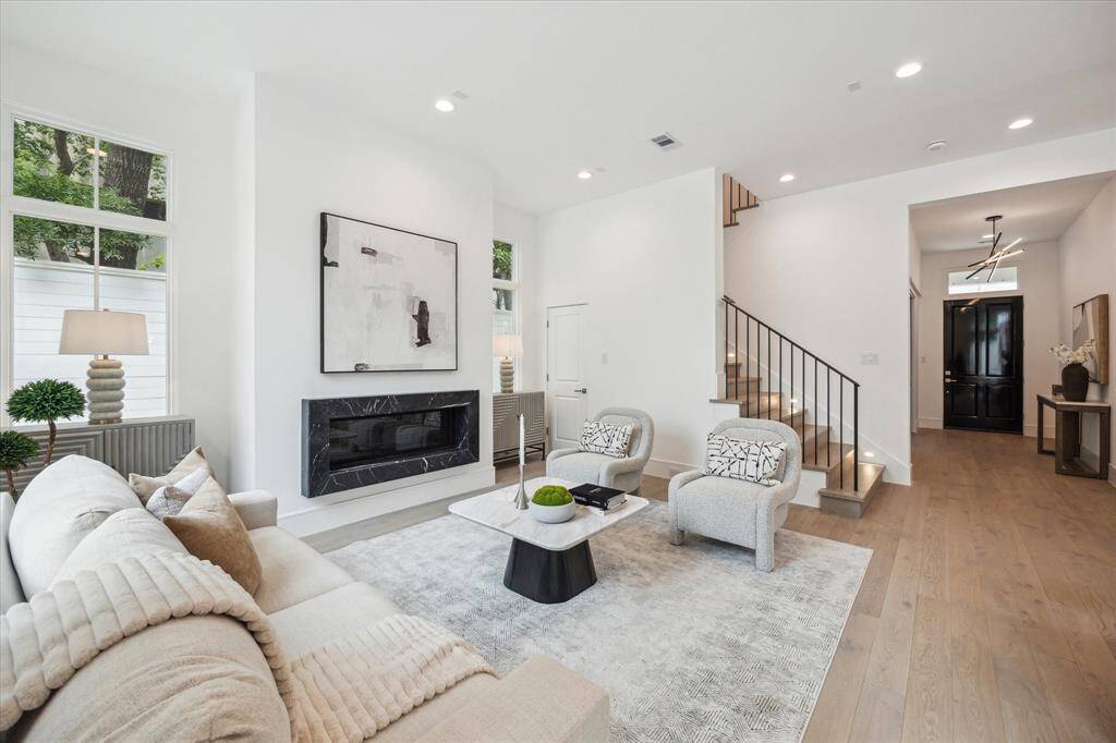 The expansive living room features an elegant fireplace with Nero Marquina detail, wrought iron stairway detail, LED integrated recessed lighting and Pella Lifestyle windows.