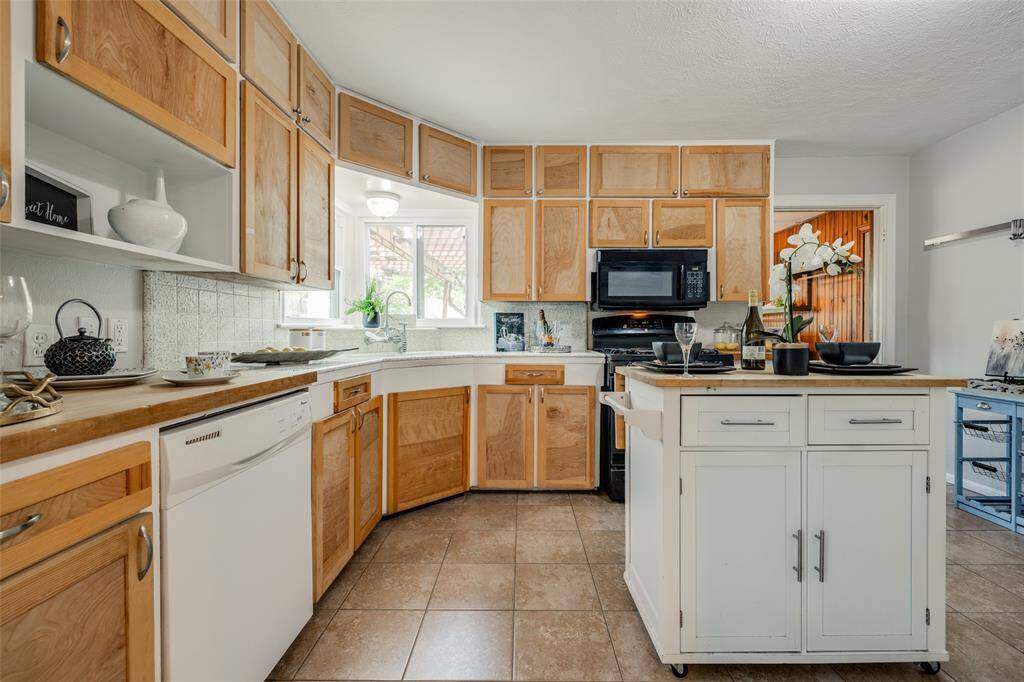 Kitchen with light wooden cabinets, white dual sink, gas cooker, microwave, dishwasher, movable center island