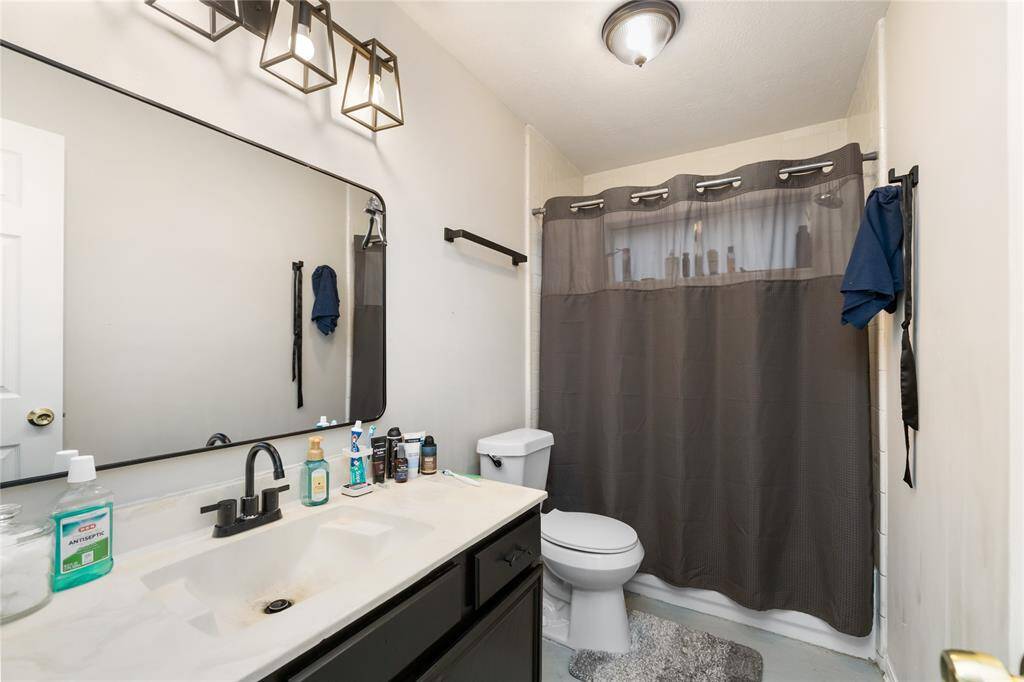 The secondary bathroom features a tub/shower combo, sleek black cabinetry with white counters, and a framed mirror—well-lit and ready for use.