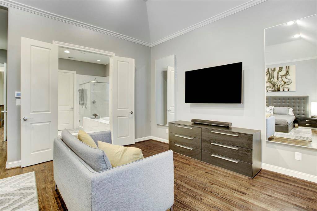 Sitting Area in Primary Suite showcases a loveseat and a dresser with TV above, and 2 large mirrors flanking the TV.  The double doors open to the sumptuous Primary EnSuite Bath & 2 Walk-in Closets.