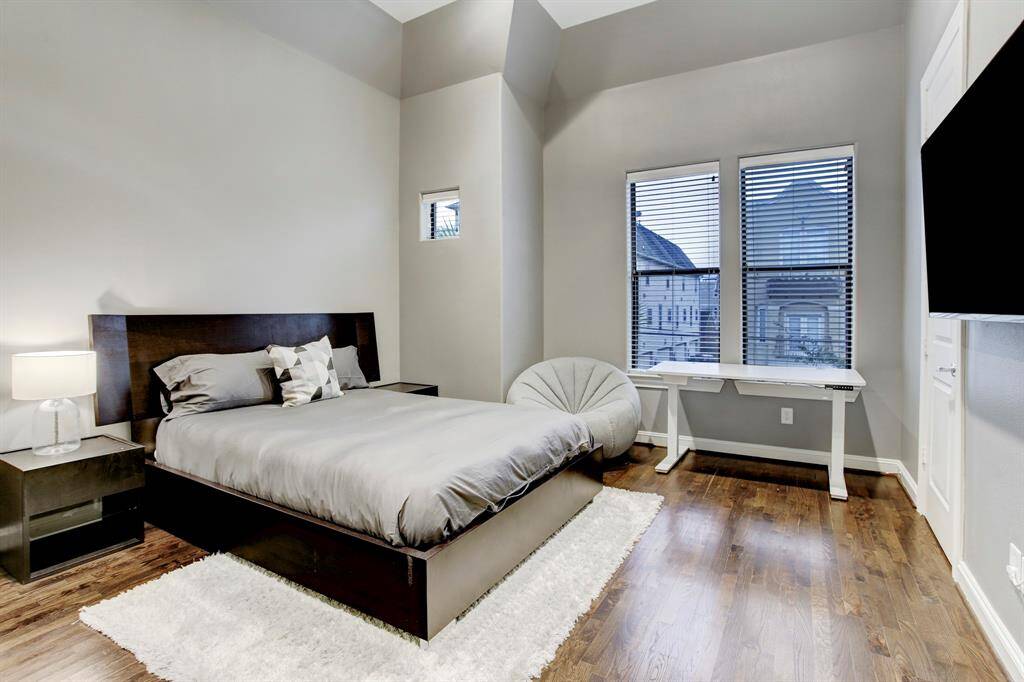 Guest Bedroom with queen-sized bed and night stands, wall-mounted TV, walk-in closet and a shared full bath.  Notice the 2 large windows, high ceiling and hardwood floor. Unseen are recessed lighting and a ceiling fan.