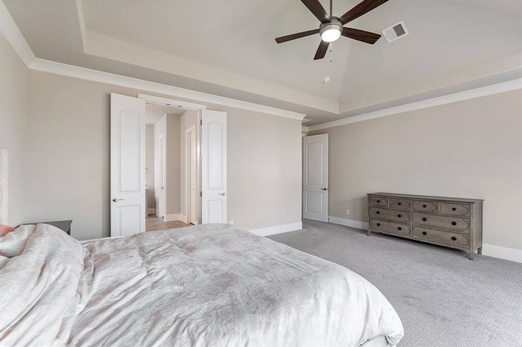 Additional view of the primary bedroom suite highlighting the double door entry to the primary bathroom. Crown molding, high ceilings and neutral finishes add sophistication to this retreat!