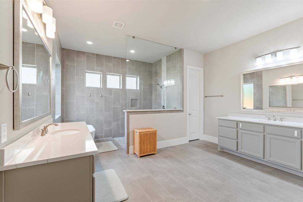This second perspective highlights the spacious double vanity, offering ample storage space for all your essentials. The large soaking tub invites you to relax and unwind, while the walk-in shower with a modern glass surround adds a touch of luxury. Upgraded lighting throughout enhances the elegance of the space, providing a spa-like ambiance that’s perfect for any time of day.
