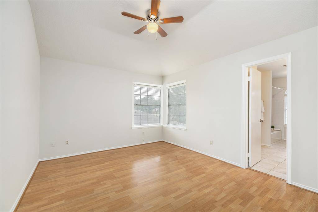 Primary bedroom has a high ceiling, ceiling fan, large windows, and no carpet.
