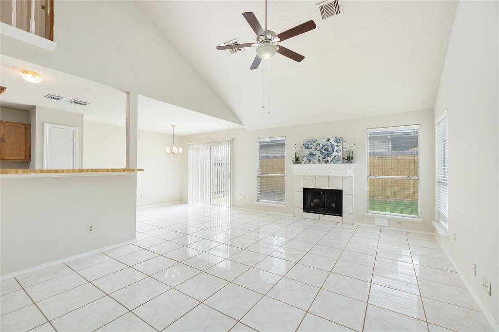 Living room has high ceilings, large windows, a centered gas log fireplace, and open to the kitchen.