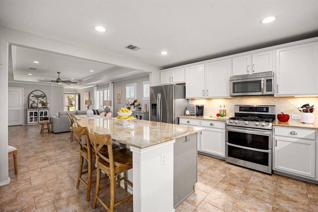 The kitchen also features custom granite, white cabinetry with elegant nickel hardware, double ovens, and a large island with seating.