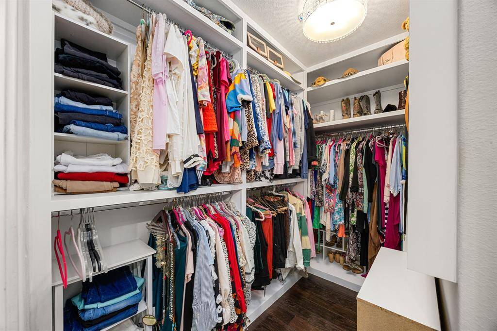 The custom built walk-in closet features ample hanging space, shelving for folded clothes, and a section for shoes and accessories, all enhanced by a stylish overhead light fixture.