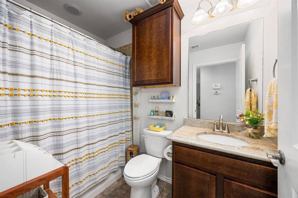 The secondary bathroom features a clean and bright granite countertop, and wood cabinetry for storage.