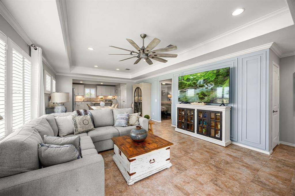 This inviting living room features a spacious layout featuring the custom wainscotting wall. It's well-lit with natural light from the windows, showcasing an open concept that flows into the kitchen area.
