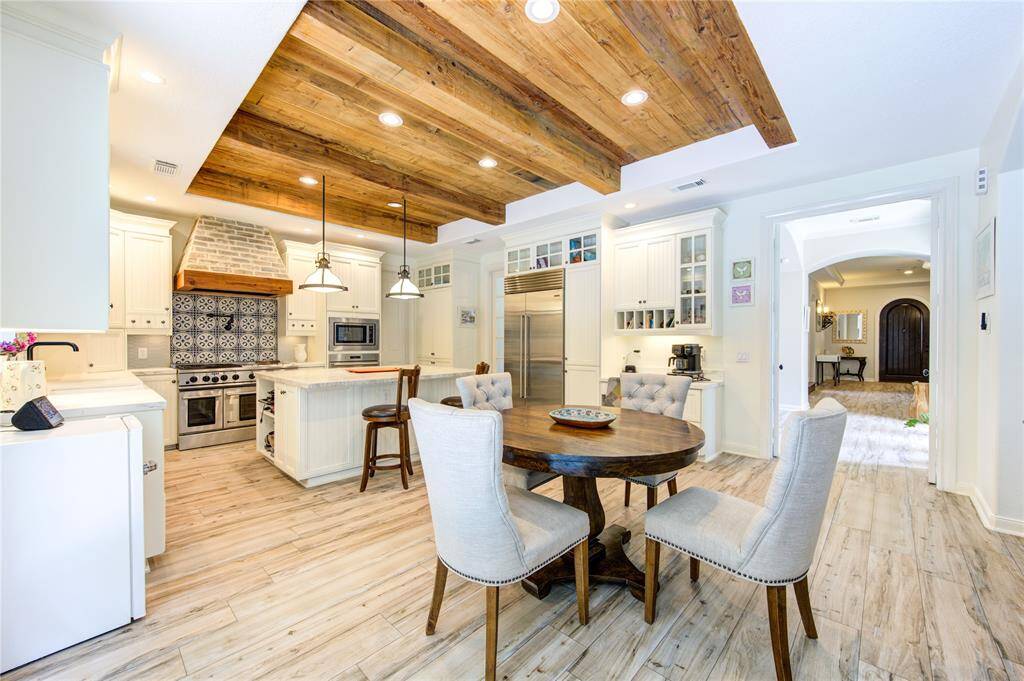 This inviting kitchen features a rustic wooden ceiling, modern appliances, and a cozy dining area. The space is bright and open, with stylish cabinetry and a charming patterned backsplash. Ideal for both cooking and entertaining.