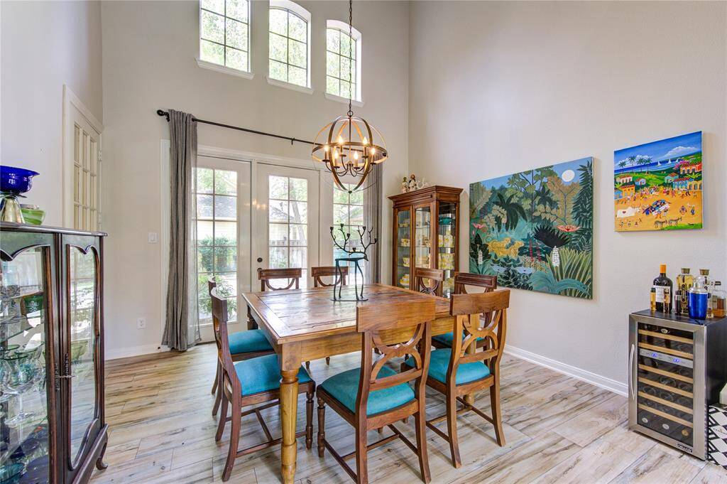 This dining area features high ceilings and large windows for plenty of natural light. It includes a wooden dining set, decorative chandelier, and vibrant wall art, creating a cozy and inviting atmosphere.