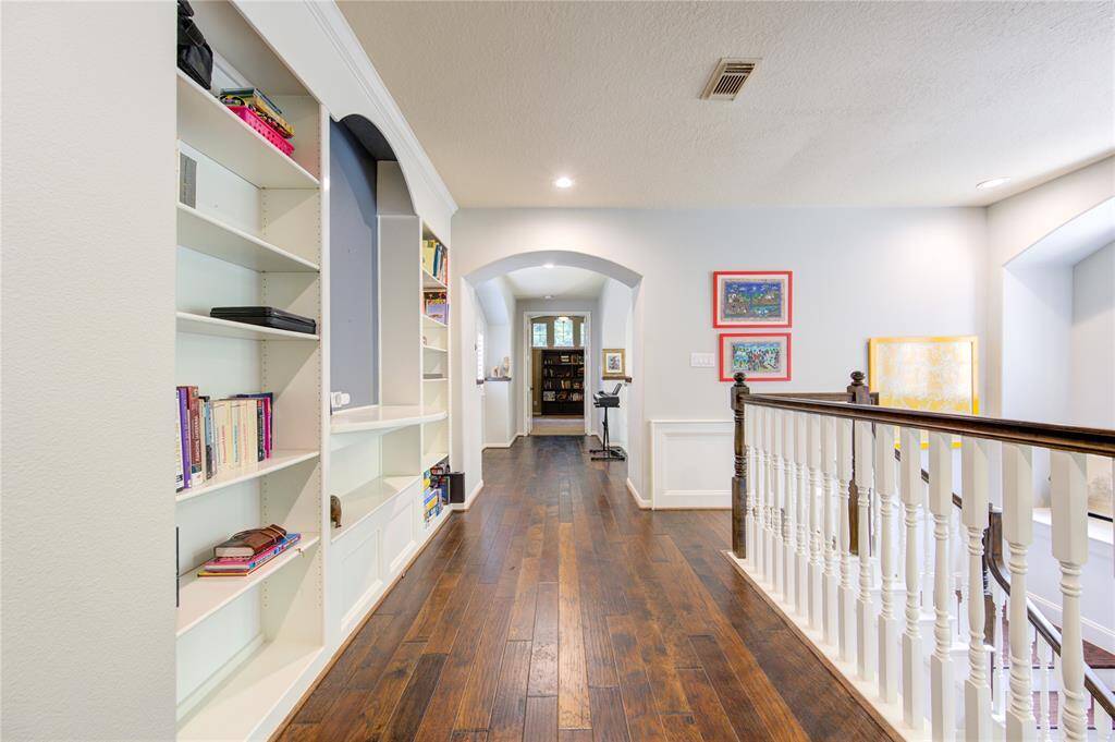 This photo showcases a bright, spacious hallway with elegant wood flooring. It features built-in bookshelves, decorative wall art, and a classic railing leading to stairs, creating a welcoming and functional space.