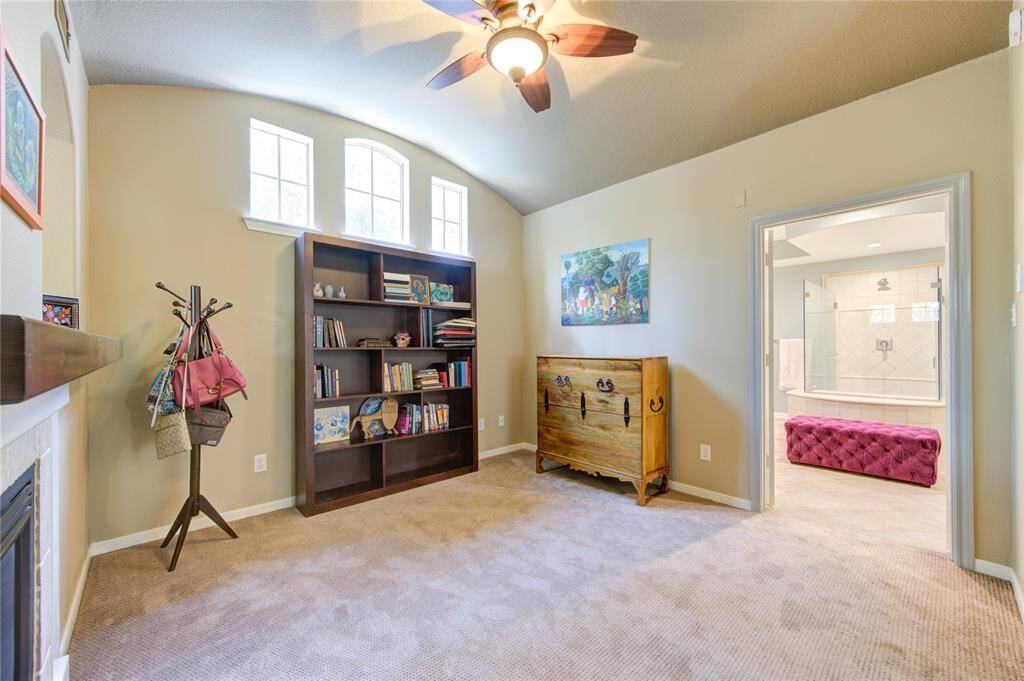 This cozy room features a vaulted ceiling with a fan, a built-in bookcase, and a fireplace. It connects to a spacious bathroom with a glass-enclosed shower and a plush seating bench, offering a comfortable and functional living space.