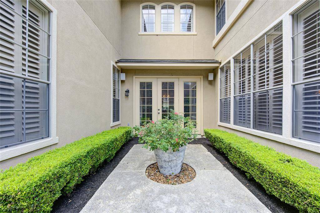 This photo showcases an inviting courtyard entrance with well-maintained hedges and a central planter. Large windows with shutters line the walls, providing ample natural light to the space.