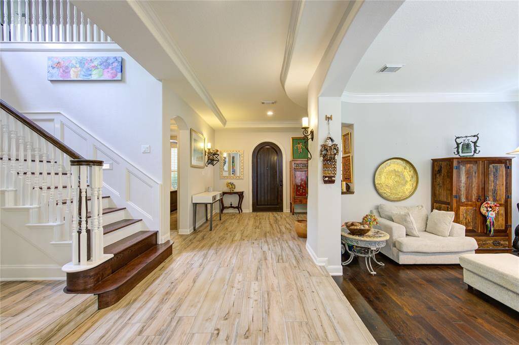 Bright, inviting entryway with elegant staircase, wood and tile flooring, and a cozy seating area. Arched doorway and tasteful decor add charm and character.