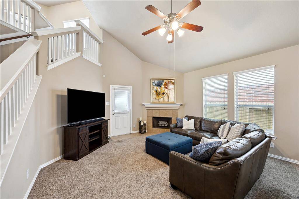Bright and inviting family room with tall ceilings, a ceiling fan, and plenty of windows for natural light. Cozy up by the fireplace or step through the back door to enjoy the covered patio—perfect for indoor-outdoor living and entertaining.