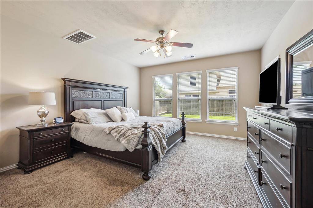 Spacious primary bedroom features a stunning wall of three windows that flood the room with natural light, a ceiling fan for added comfort, and a large ensuite bath offering dual sinks, a soaking tub, and a separate shower for a luxurious retreat.