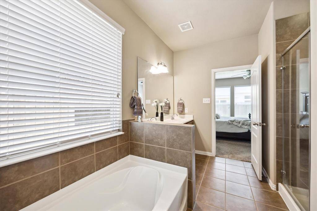 Another view of the primary bath showcases a large soaking tub beneath a bright window, complemented by a spacious walk-in shower. This serene space offers both natural light and modern comforts for a relaxing experience.
