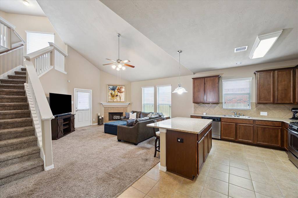 Spacious kitchen and family room combo features soaring ceilings, a cozy fireplace, and a welcoming staircase with elegant California wood rails. The open layout is perfect for gatherings, offering style, comfort, and seamless flow throughout the main living area.