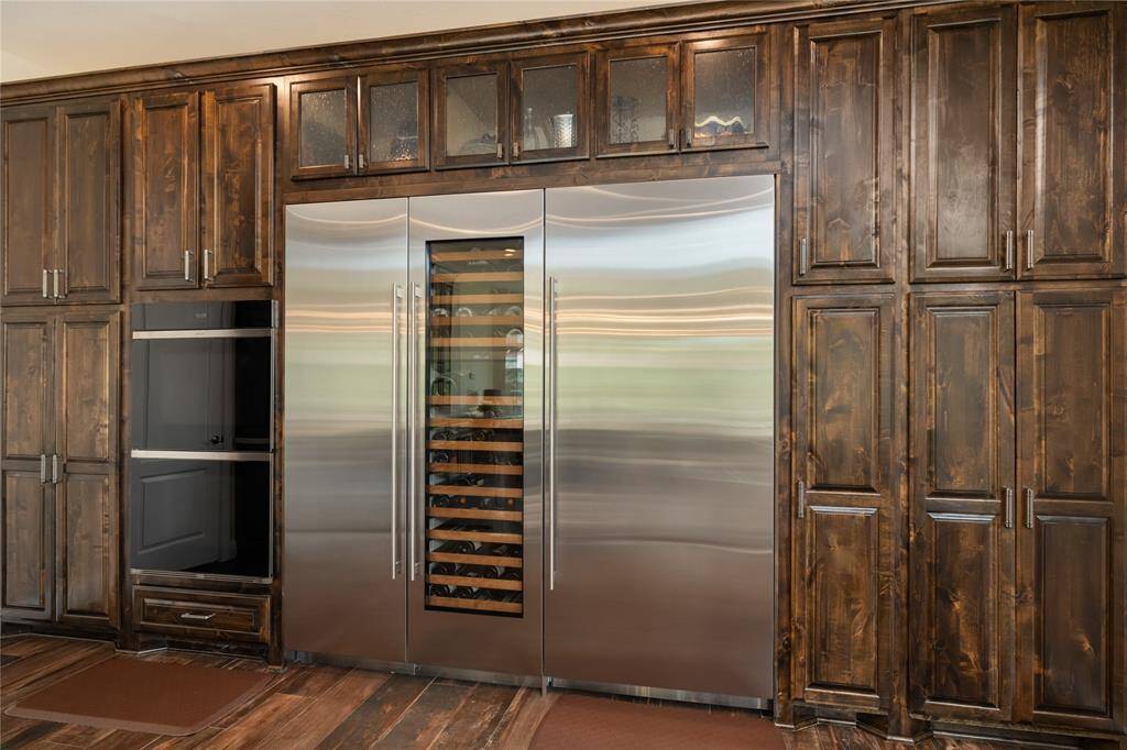 Built-in double ovens, a sleek refrigerator, and a wine fridge are seamlessly integrated into rich, dark wood cabinetry, setting a stately tone in this chef-caliber kitchen. Stainless steel appliances complement the refined aesthetic while offering top-tier functionality.